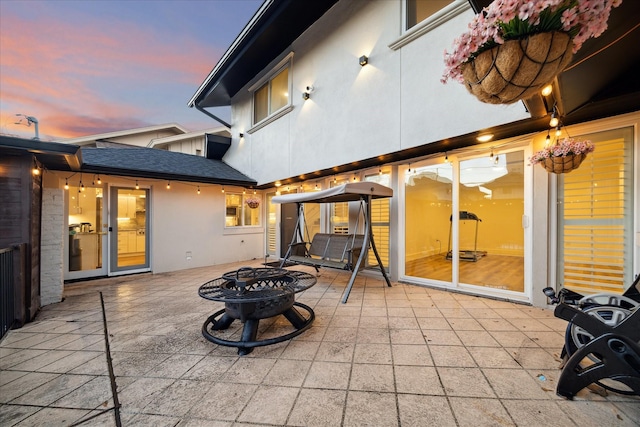 back of property featuring a fire pit, roof with shingles, a patio area, and stucco siding