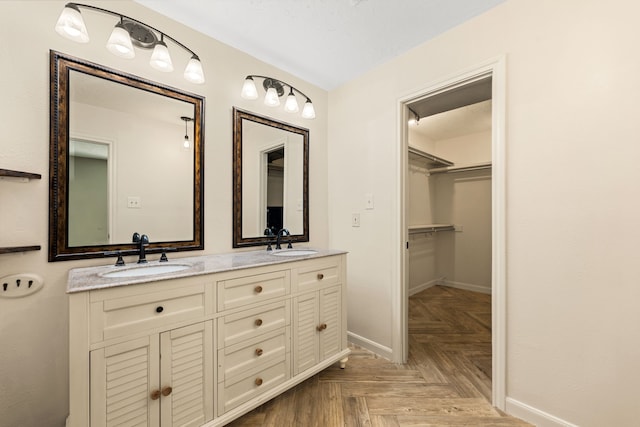 full bathroom with double vanity, a sink, a walk in closet, and baseboards