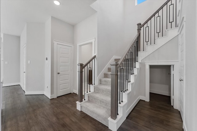 staircase featuring a towering ceiling, baseboards, wood finished floors, and recessed lighting