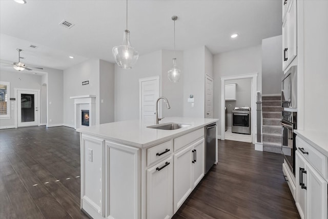 kitchen featuring white cabinets, open floor plan, a kitchen island with sink, light countertops, and a sink