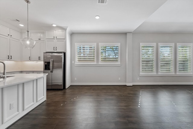 kitchen featuring stainless steel fridge, white cabinets, hanging light fixtures, light stone countertops, and a sink