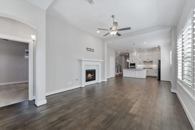 unfurnished living room with a healthy amount of sunlight, a lit fireplace, dark wood-style flooring, and a ceiling fan