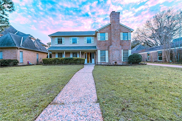 traditional home with a chimney, a lawn, and brick siding