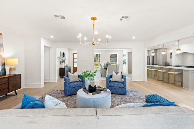 living area with an inviting chandelier, light wood-style flooring, and visible vents