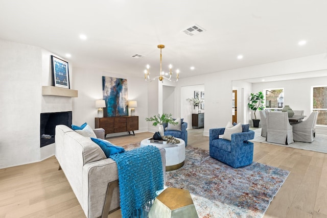 living room featuring an inviting chandelier, light wood-style flooring, a fireplace, and visible vents