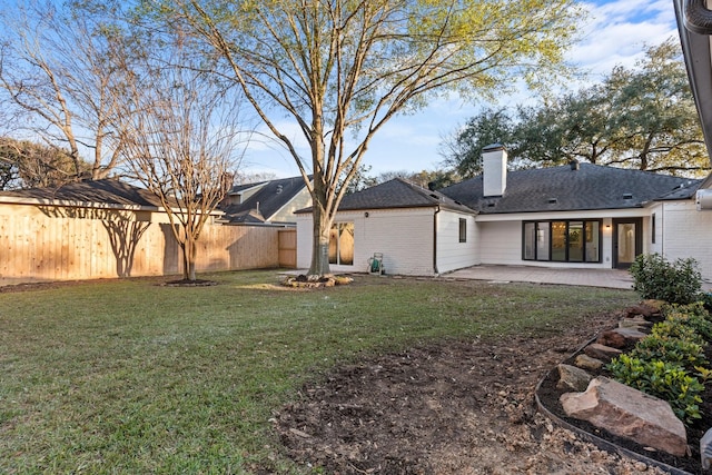 back of property featuring a fenced backyard, brick siding, a yard, a chimney, and a patio area