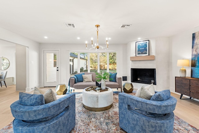 living area featuring light wood-type flooring, a fireplace, visible vents, and an inviting chandelier