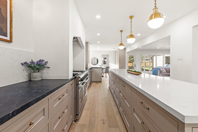 kitchen with stainless steel range, open floor plan, dark stone countertops, hanging light fixtures, and light wood-style floors