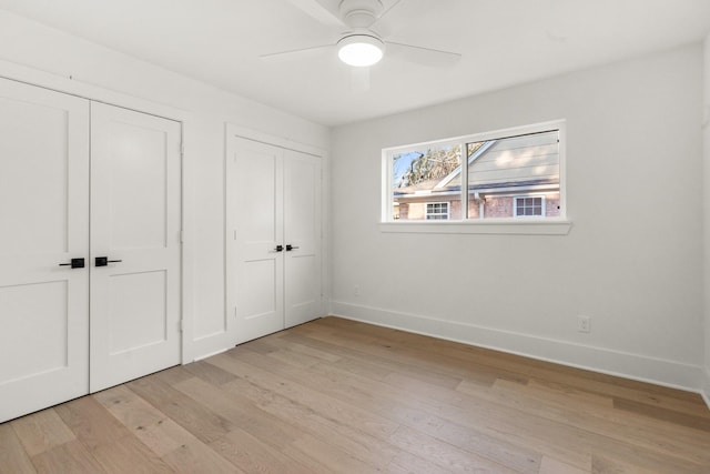 unfurnished bedroom featuring light wood-type flooring, a ceiling fan, baseboards, and two closets