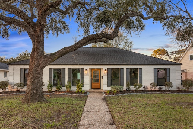 view of front of home with roof with shingles, a yard, and brick siding