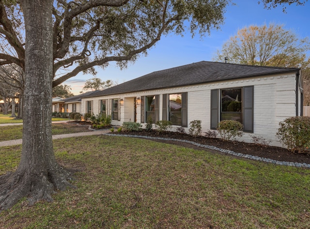 single story home featuring a front yard, brick siding, and roof with shingles