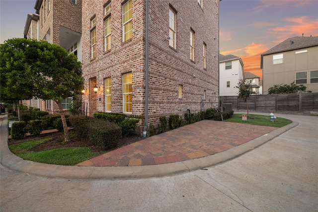 property exterior at dusk featuring brick siding and fence