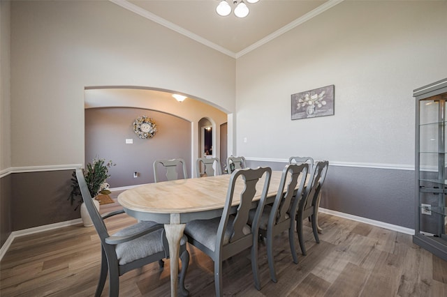 dining space with arched walkways, baseboards, wood finished floors, and crown molding