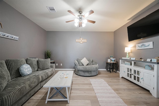 living room with light wood-style flooring, visible vents, ceiling fan, and baseboards