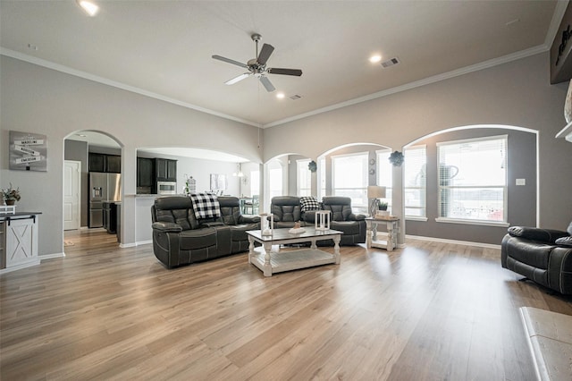 living room featuring light wood finished floors, baseboards, visible vents, ceiling fan, and crown molding