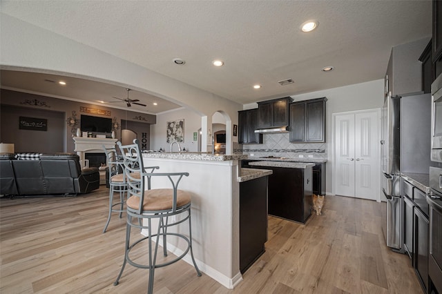 kitchen with arched walkways, a fireplace, a breakfast bar area, open floor plan, and a kitchen island