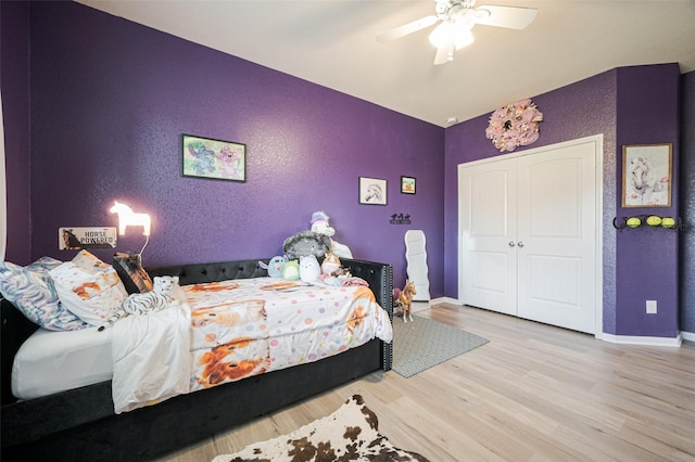 bedroom featuring a textured wall, a ceiling fan, baseboards, a closet, and light wood-type flooring