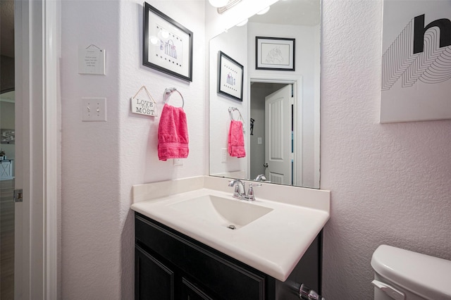 bathroom with toilet, a textured wall, and vanity