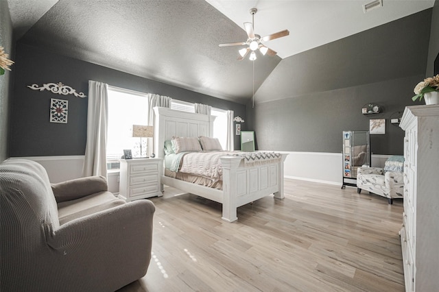 bedroom with light wood-type flooring, lofted ceiling, visible vents, and a textured ceiling