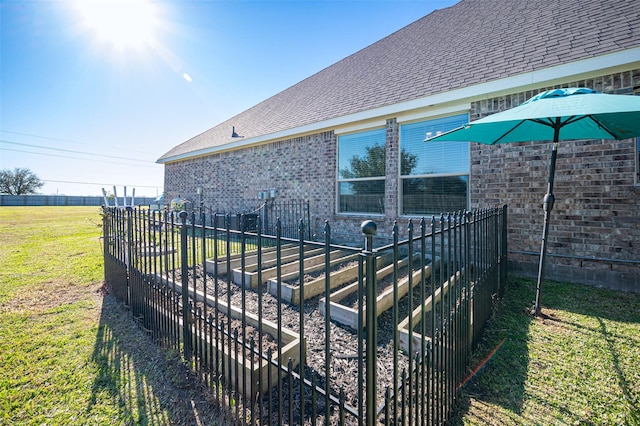 view of side of property with brick siding, fence, a garden, roof with shingles, and a lawn