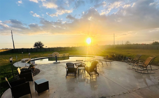 patio terrace at dusk with a lawn, fence, and a fenced in pool