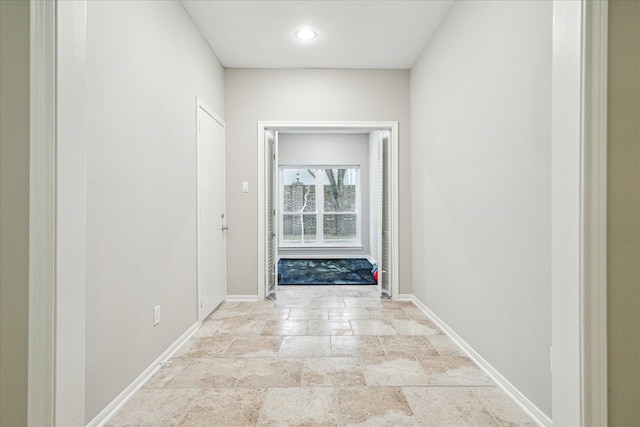 corridor featuring stone finish floor and baseboards