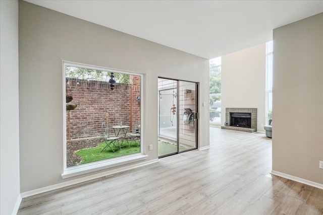 unfurnished room featuring baseboards, a brick fireplace, and light wood-style floors