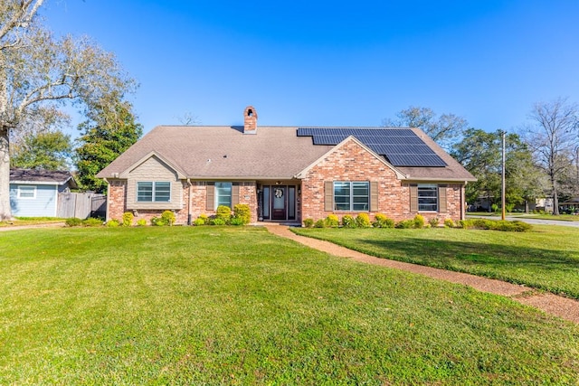 view of front of property with brick siding, roof with shingles, roof mounted solar panels, a front lawn, and a chimney