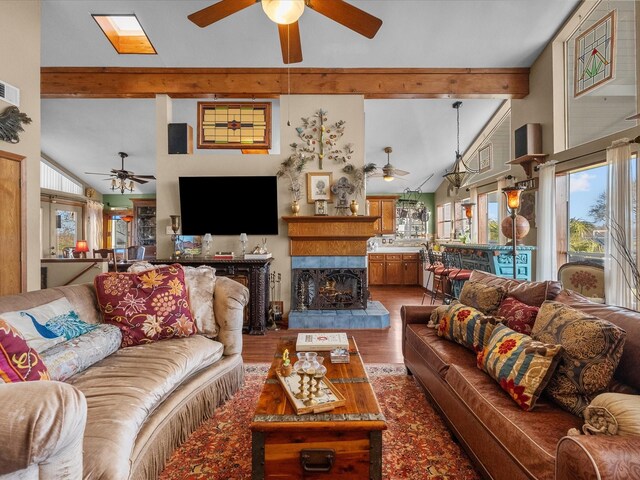 living area featuring lofted ceiling with beams, a fireplace with raised hearth, wood finished floors, and a ceiling fan