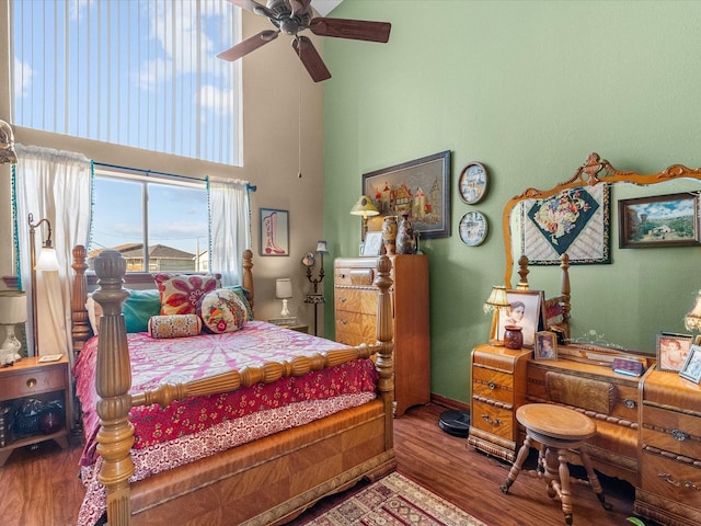 bedroom with a towering ceiling, ceiling fan, baseboards, and wood finished floors