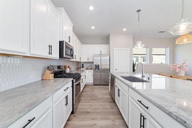 kitchen with light stone counters, hanging light fixtures, stainless steel appliances, white cabinetry, and a sink
