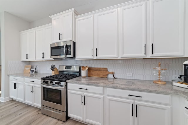 kitchen featuring stainless steel appliances, tasteful backsplash, white cabinets, and light stone countertops