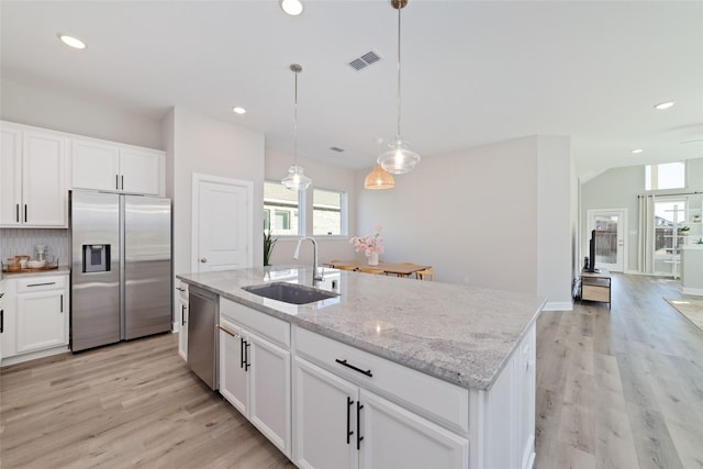 kitchen featuring a sink, white cabinets, appliances with stainless steel finishes, an island with sink, and decorative light fixtures