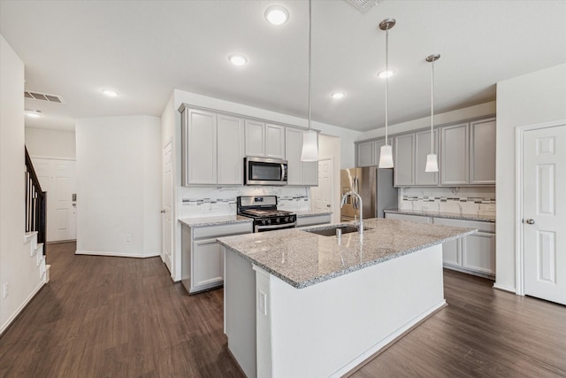 kitchen with a sink, appliances with stainless steel finishes, a center island with sink, light stone countertops, and decorative light fixtures