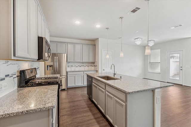 kitchen featuring stainless steel appliances, visible vents, hanging light fixtures, a kitchen island with sink, and a sink