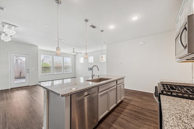 kitchen featuring light stone counters, a kitchen island with sink, stainless steel appliances, a sink, and hanging light fixtures