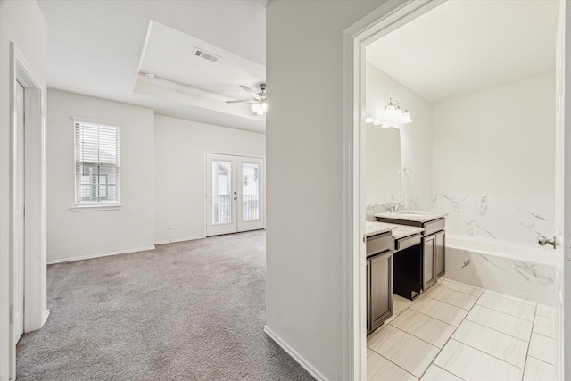 interior space with baseboards, visible vents, light colored carpet, a tray ceiling, and french doors