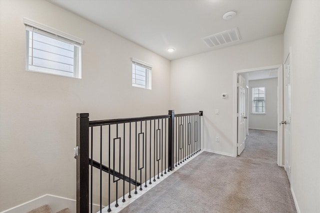 corridor with baseboards, plenty of natural light, visible vents, and light colored carpet