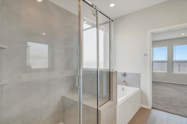 bathroom with a garden tub, a shower stall, baseboards, and wood finished floors