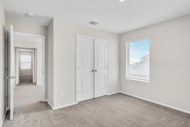 unfurnished bedroom featuring a closet, light carpet, visible vents, and baseboards