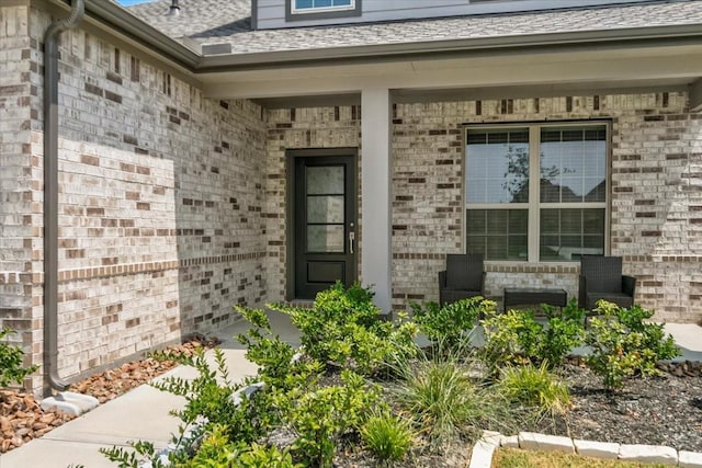 doorway to property with brick siding and roof with shingles