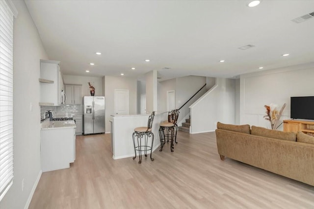 kitchen featuring stainless steel appliances, white cabinetry, open floor plan, light countertops, and light wood finished floors