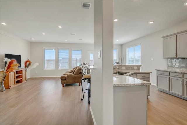 kitchen with light wood-style flooring, visible vents, open floor plan, light stone countertops, and tasteful backsplash