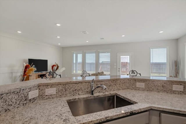 kitchen with a wealth of natural light, a sink, recessed lighting, and light stone countertops