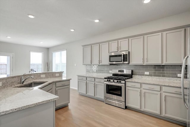 kitchen with gray cabinetry, appliances with stainless steel finishes, decorative backsplash, and light stone countertops