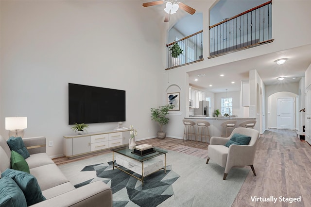 living room with light wood-type flooring, baseboards, arched walkways, and a ceiling fan