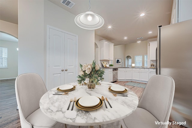 dining room with arched walkways, wood finished floors, visible vents, and recessed lighting