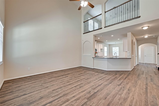 unfurnished living room with arched walkways, a sink, baseboards, and wood finished floors