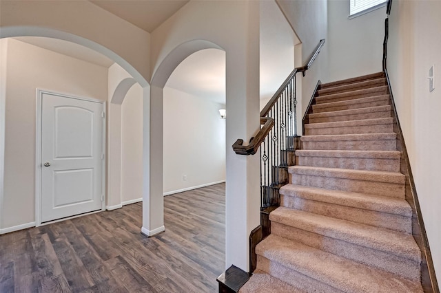 stairs with arched walkways, baseboards, and wood finished floors