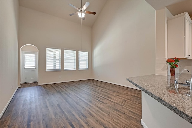 unfurnished living room featuring dark wood-style floors, baseboards, high vaulted ceiling, and ceiling fan